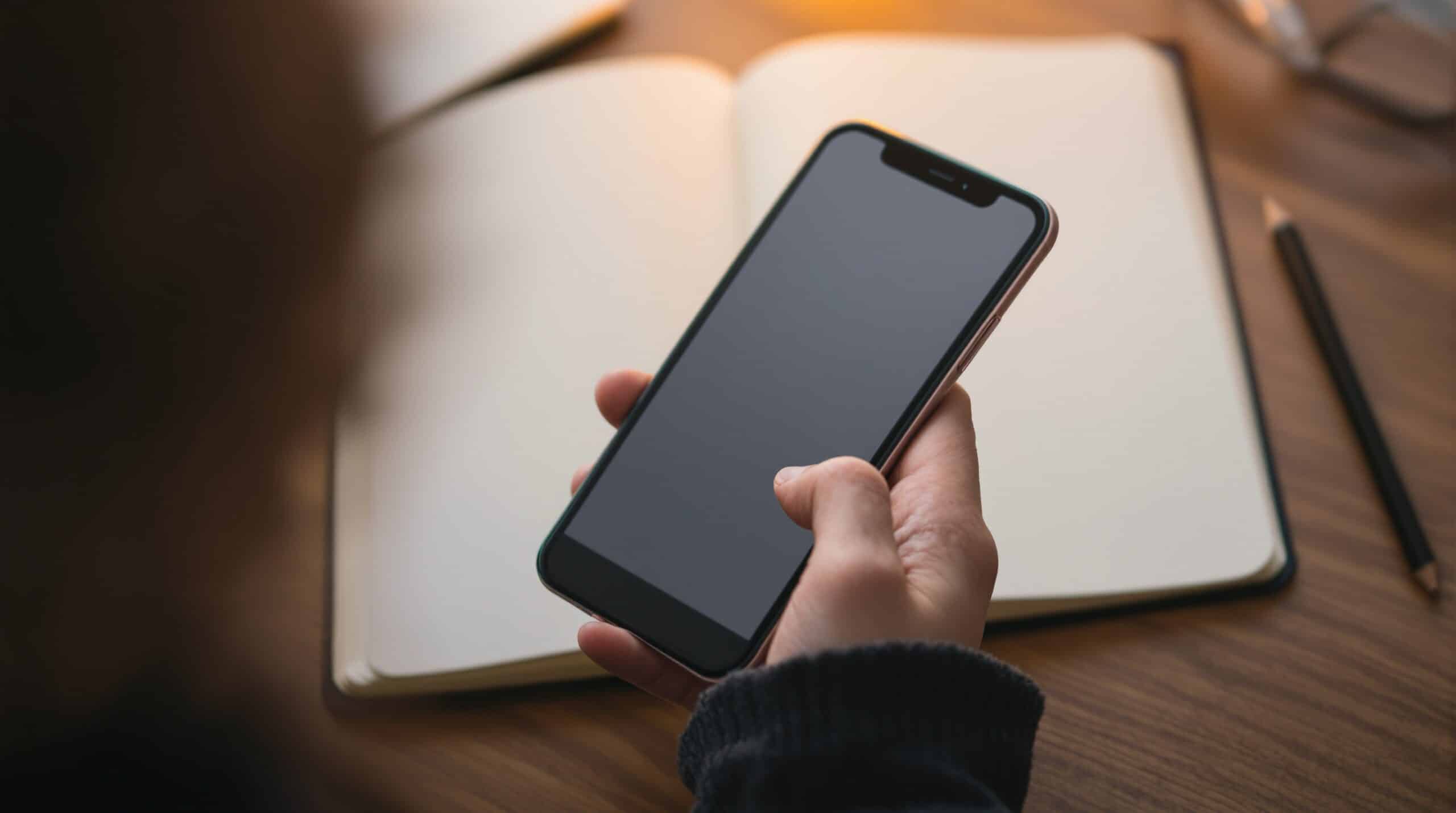 Hands holding smartphone with note app next to open journal on wooden table, showing digital journaling alternatives